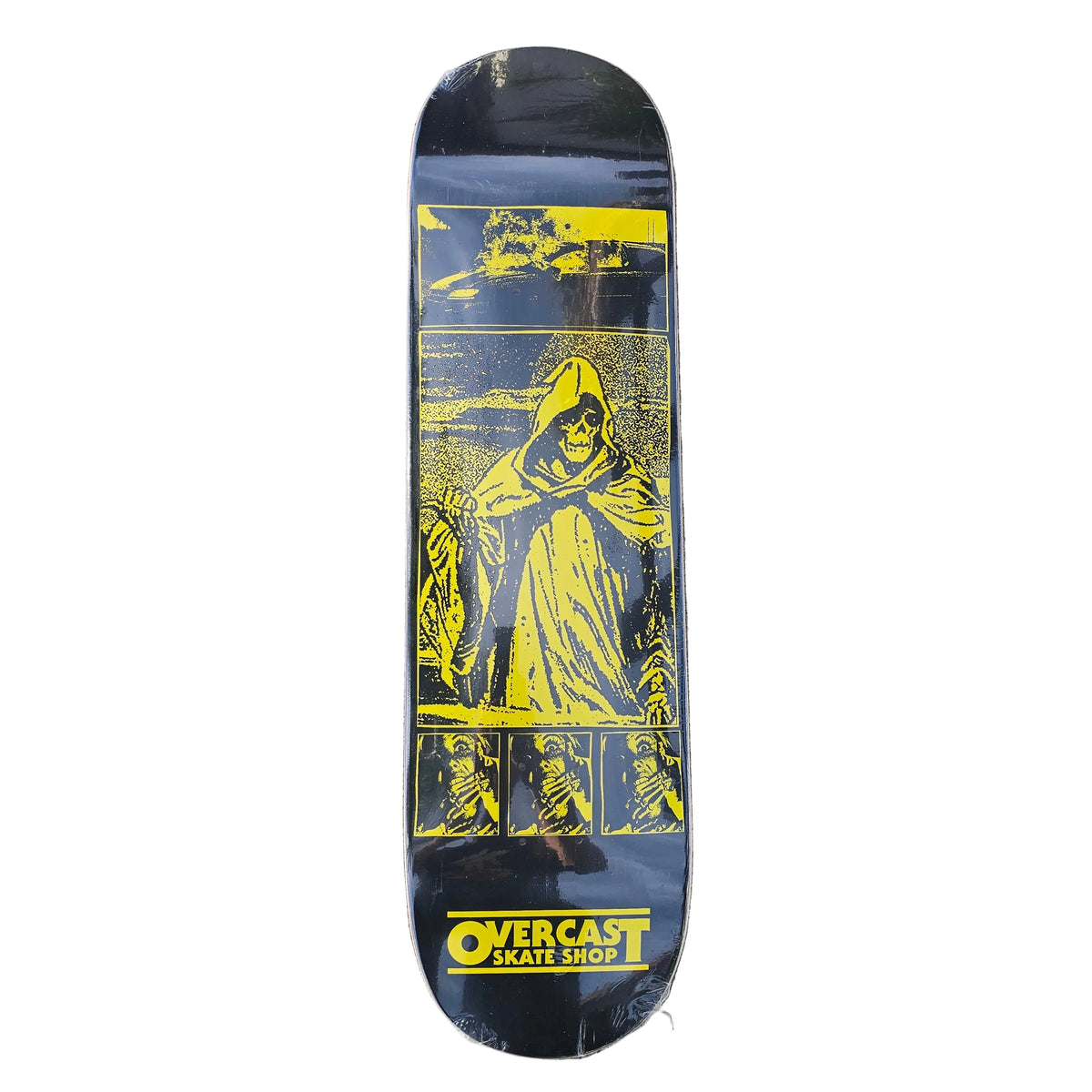 A skateboard deck with a black background and a bold yellow graphic of a hooded skeleton, photographed flat on a gray concrete surface. The brand name 'Overcast Skate Shop' is printed in yellow at the bottom.